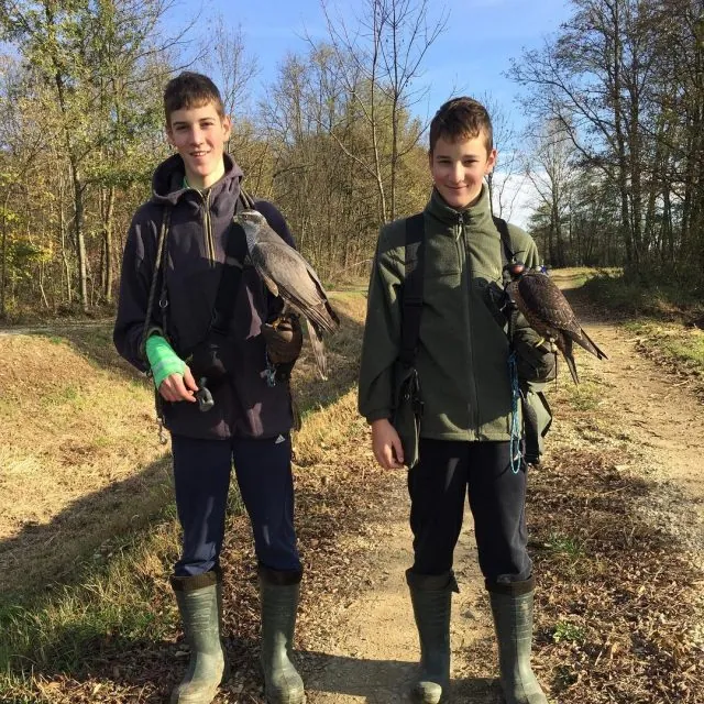 Two boys in wellington boots holding falcons on a woodland track in autumn